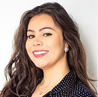 Laura Hmelo Jawad Branding Woman sitting with crossed legs on a couch, chin resting on hand, with a laptop and a water bottle nearby, in a casual indoor setting.