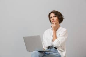 Thinking woman sitting on stool holding laptop computer.
