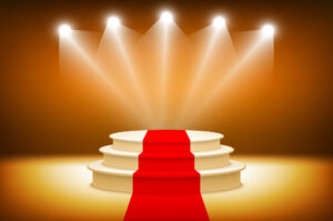 An illuminated stage with spotlights and a red carpet leading to a circular podium on an amber background.